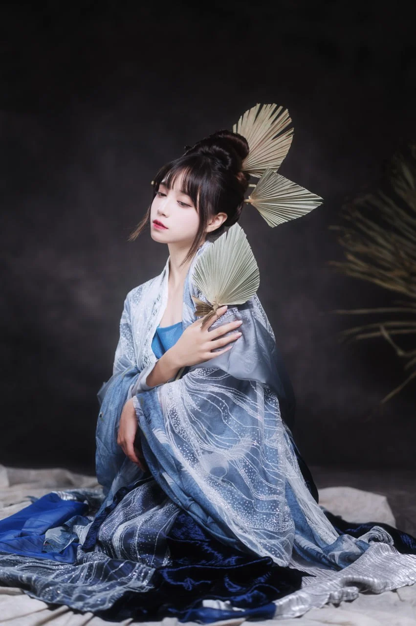 暖调灯光下，黑发女子盘着繁复发髻配金色流苏，身披红蓝绿拼色的华丽花纹和服，右肩半露，身后有红色圆形背景板