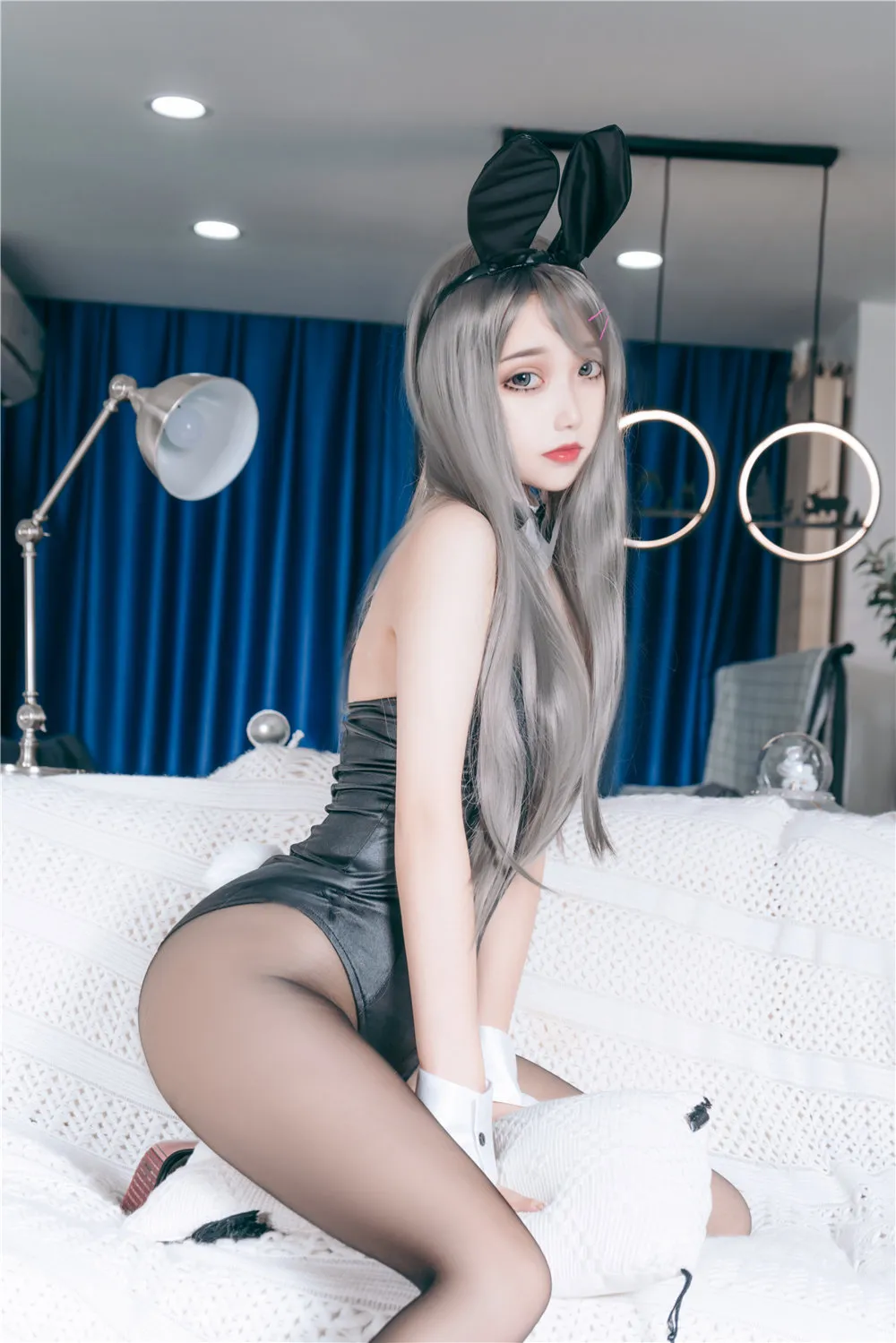 Eloise软软室内床上,银灰长发女子头戴黑色兔耳发箍,身穿黑色紧身连体亮面皮衣和黑色丝袜,双手戴白色短手套撑在白色针织毯上,跪姿看向镜头
