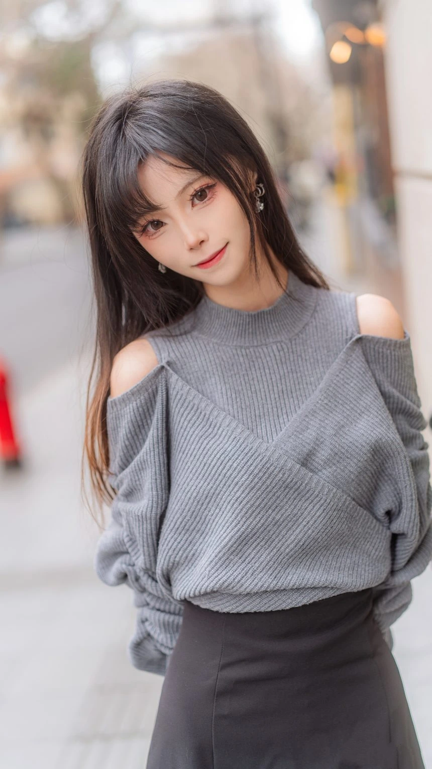 坂坂白在街景虚化背景灰色针织上衣站姿出镜，长发与肩部剪裁细节清晰