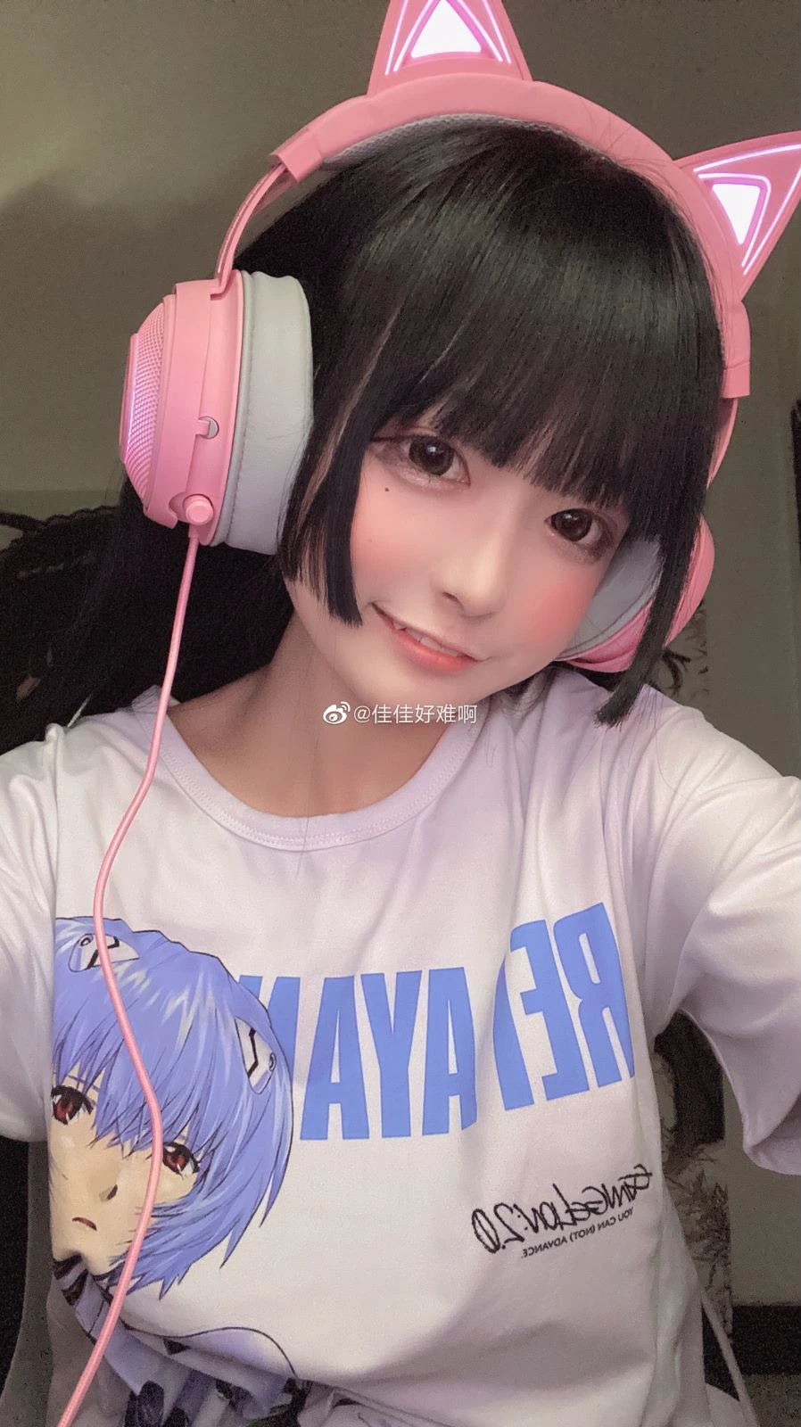 佳佳好难啊在室内近景画面里近景微笑出镜，粉色猫耳耳机与白色印花T恤细节清晰