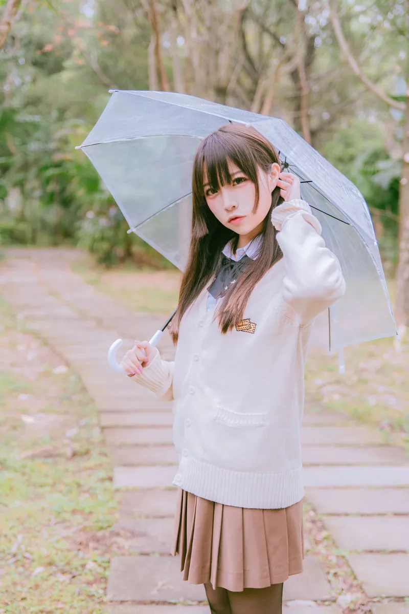 二佐Nisa身穿浅色校园针织衫与百褶裙，在林间小路手持透明雨伞拍摄