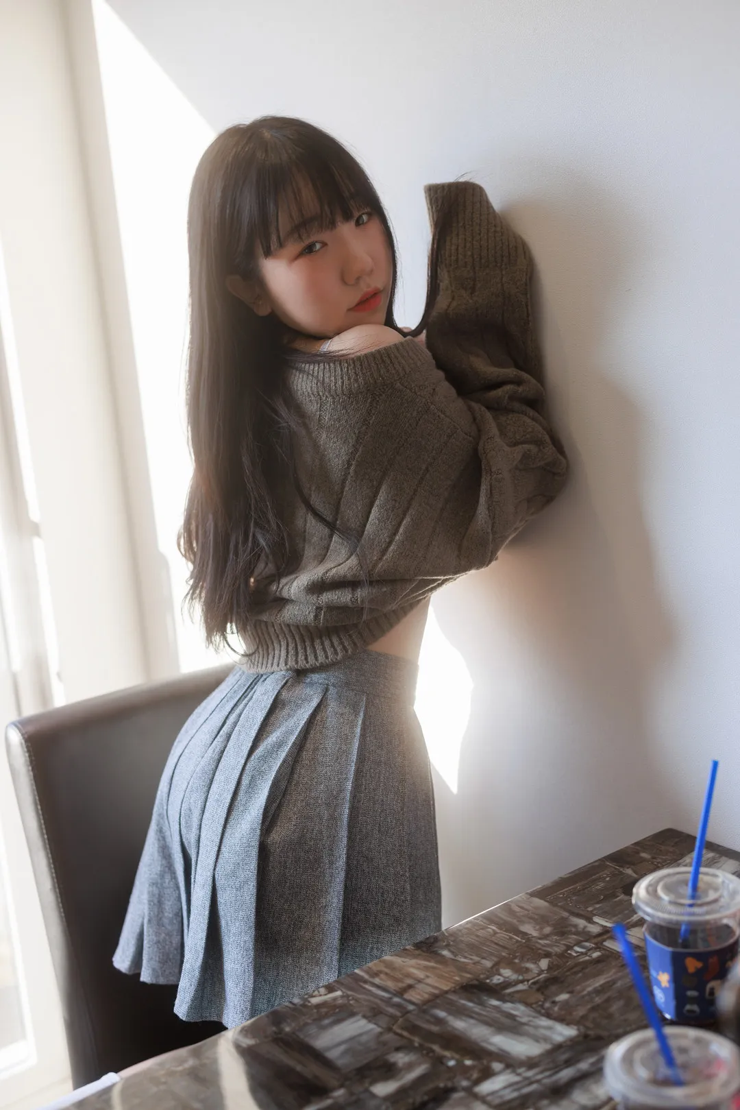 Yeri 灰色毛衣百褶裙站在白墙和咖啡桌旁