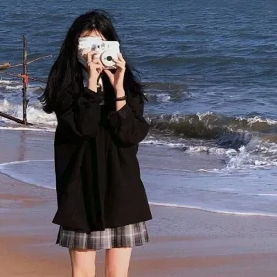 nide_xiaogou穿黑色宽松上衣和格纹短裙站在海边，双手举相机遮住面部