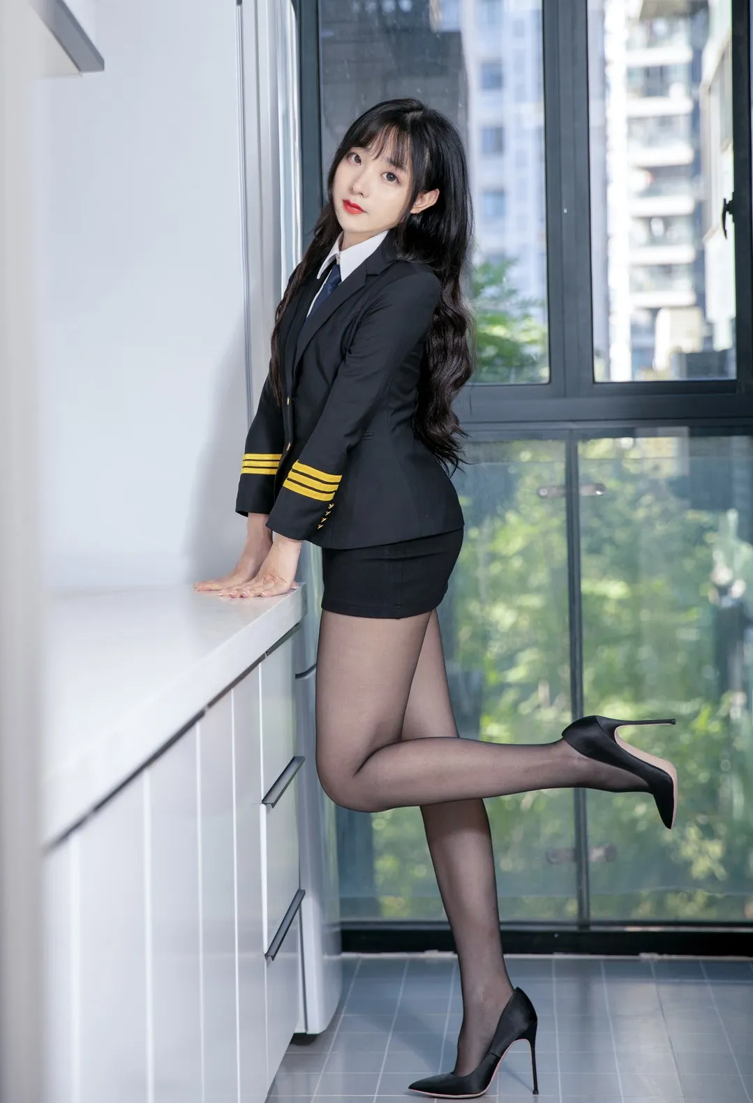 豪歌 长发穿黑色制服和高跟鞋在窗边扶台面站立