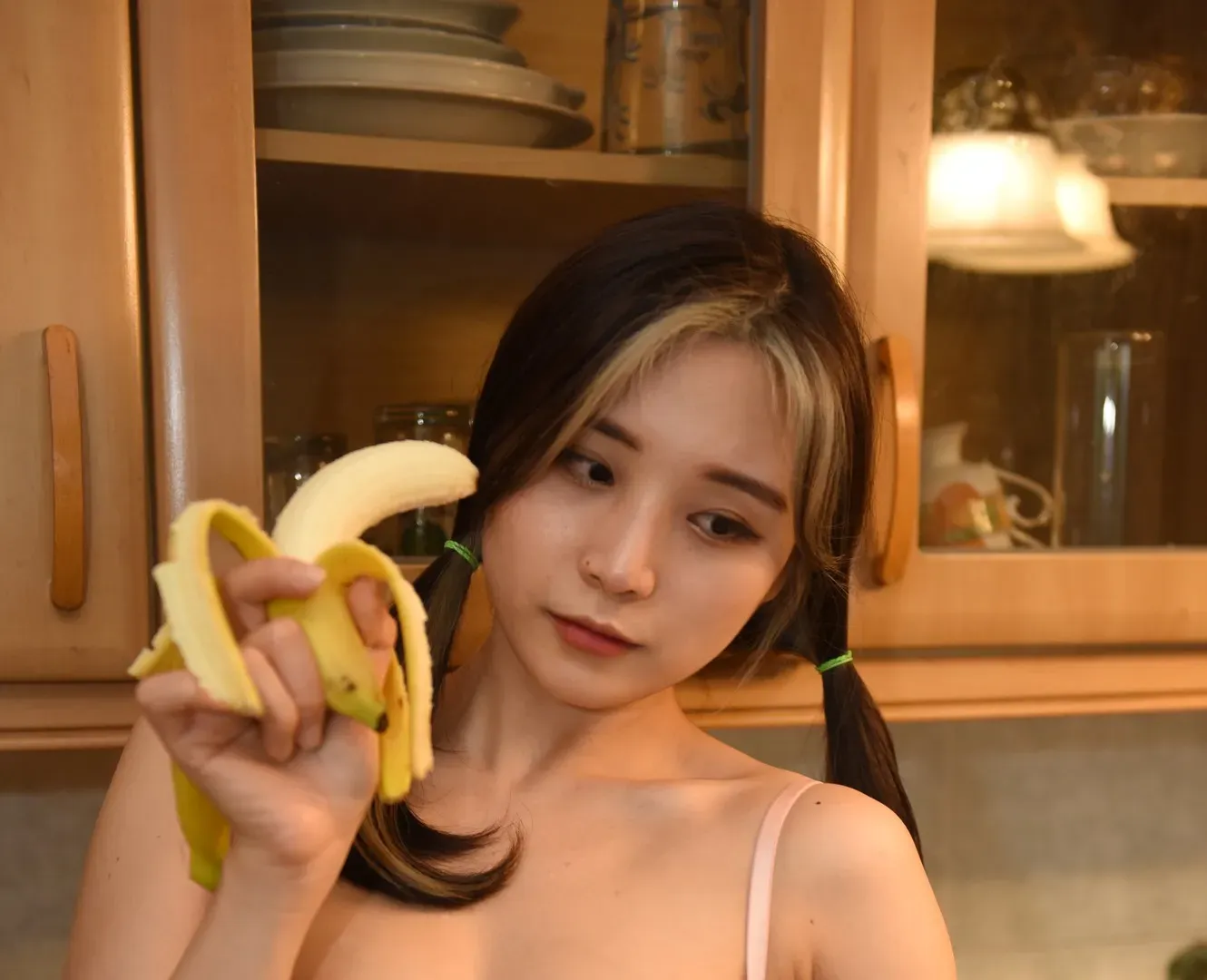 GGotBBang扎双马尾坐在厨房橱柜前，手拿剥开的香蕉看向一侧的生活流写真