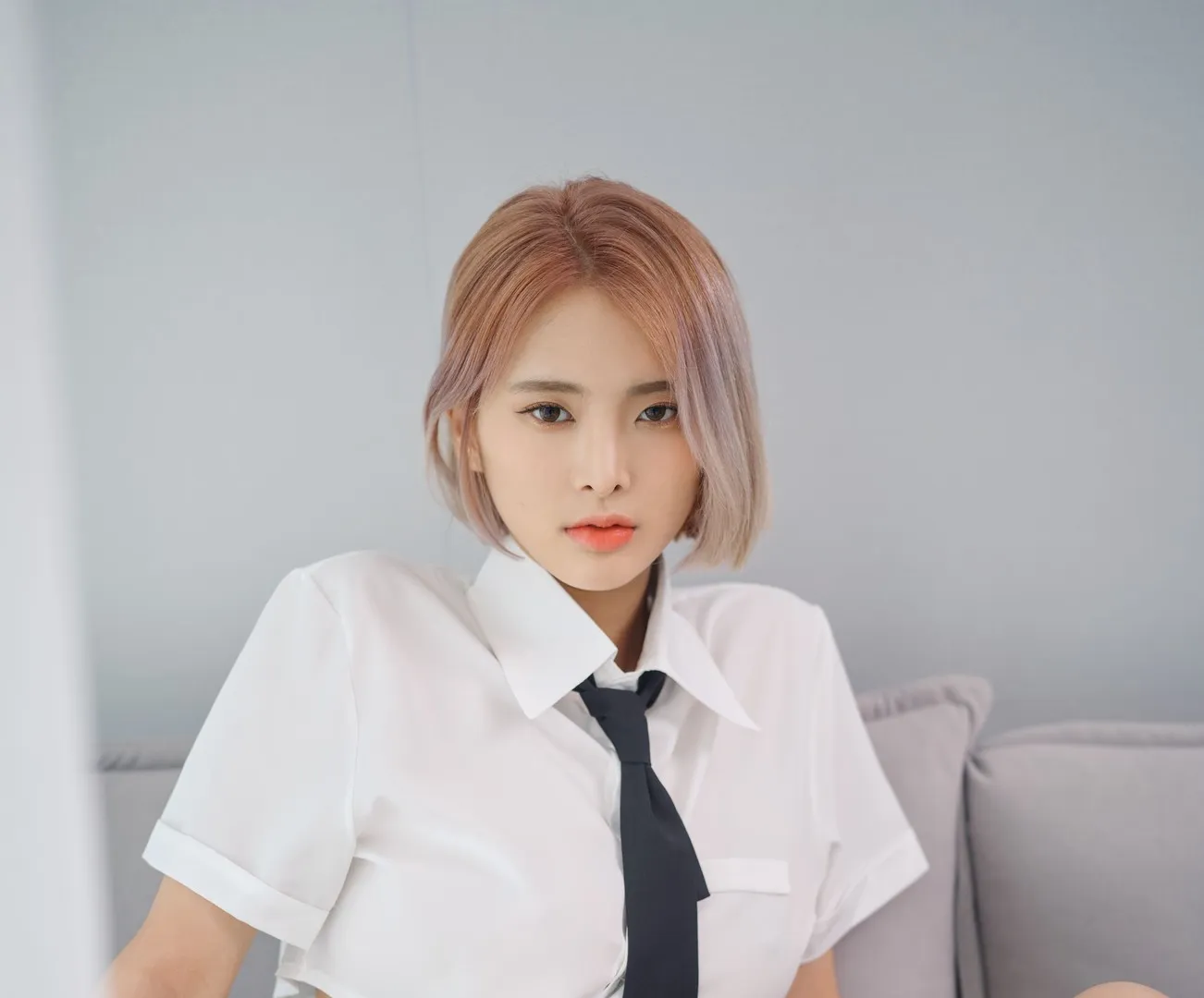 Hyoyeon(김효연) 粉色短发穿白色短袖衬衣和黑色领带坐在浅灰沙发前