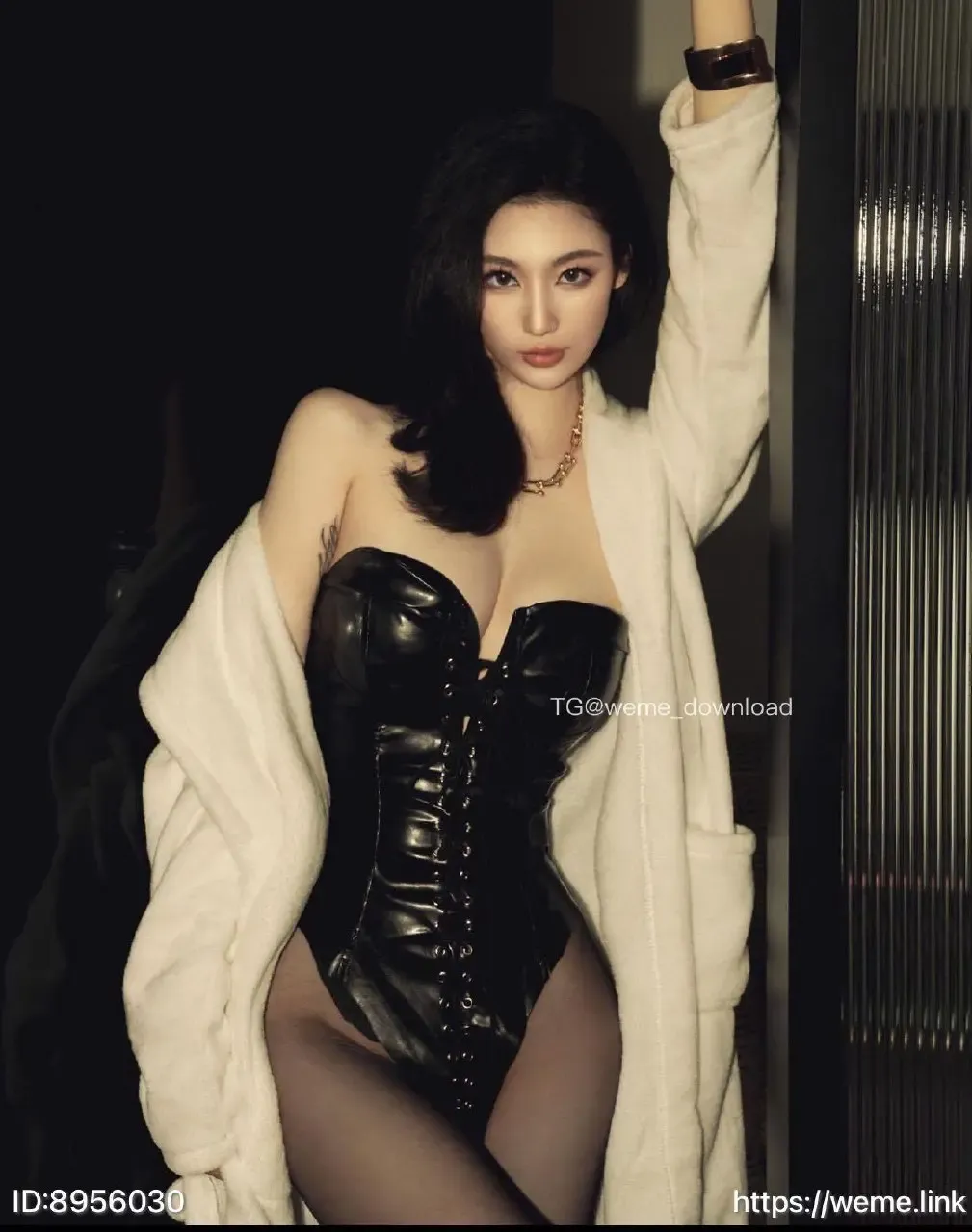 米米子呀(Maymay)穿黑色亮面连体服和乳白色外套站在深色室内背景前，手臂抬起