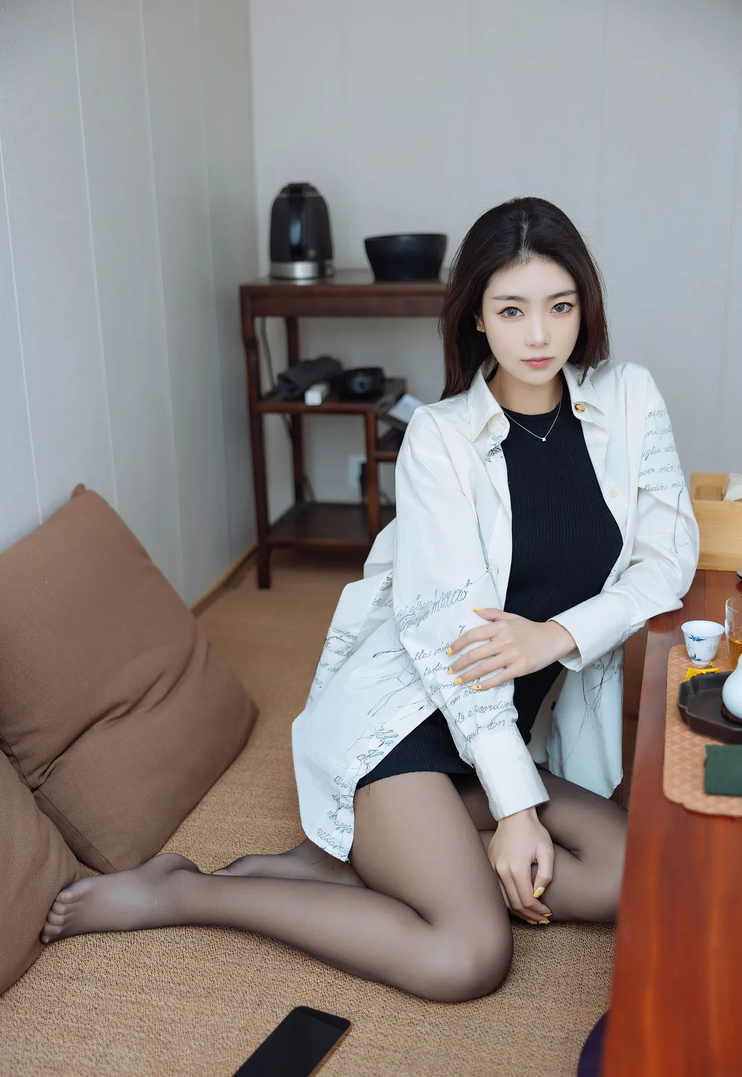 可乐Vicky长发穿白色衬衫外套和黑色连衣裙坐在室内地毯上,旁边有茶几和靠垫