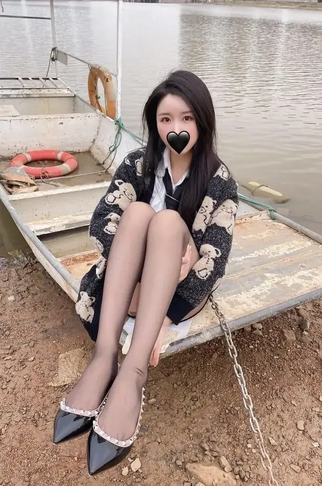 软妹小九九(July芝岚)黑色长发,穿黑白毛衣外套和黑色短裙坐在湖边船只旁