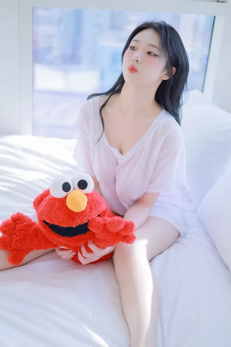 清月已经不困了穿白色衬衫坐在床边抱红色毛绒玩偶的写真
