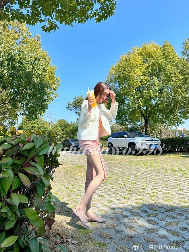 一只哈比猪户外写真，手持饮品站立于绿植旁的远景构图